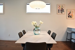 A dining area with a marble table, six chairs, a vase with flowers, a hanging light fixture, and two framed artworks on the wall.