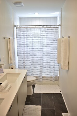 A bathroom with a white sink, toilet, and shower curtain. - The Worth Modern: Downtown 3BR home (Raleigh)