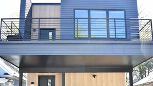 Ett modernt hus i två våningar med en täckt veranda, en väl synlig ytterdörr och en liten trädgårdsyta.