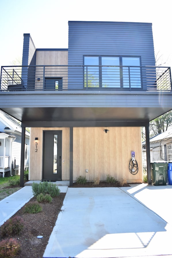 A modern two-story house with a covered front porch, a visible door, and a small garden area.