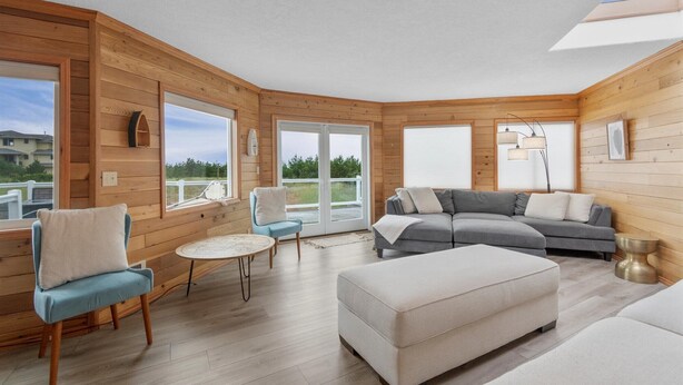 Intérieur moderne d’une cabane en rondins, avec un canapé d’angle gris, un fauteuil bleu et un pouf blanc.