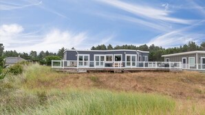 Une maison moderne dotée d’une terrasse, de grandes fenêtres et offrant une vue sur le paysage environnant.