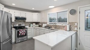 A modern kitchen with white cabinets, stainless steel appliances, a large island, and a window with blinds. - 30 NIGHT MINIMUM, Fenced Yard, firepit, near town (CCozy) (Long Beach)