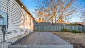 A wooden deck with a metal railing, a utility box, and a tree in the background.