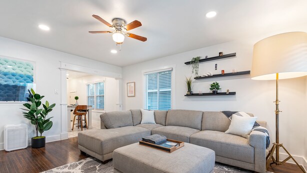A living room with a sectional sofa, a ceiling fan, a floor lamp, and a potted plant.