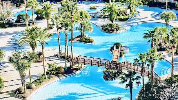 Un resort con varias piscinas, palmeras y un puente de madera.