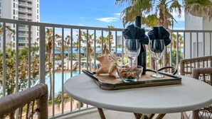Un balcón con una mesa preparada para dos personas, que incluye un cuenco de vidrio con nueces, dos vasos y una botella, además de una concha marina.