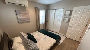 A bedroom with a bed, a window with curtains, a door, and an air conditioning unit on the wall. - Chic & intimate 2 bedroom (Brighton)