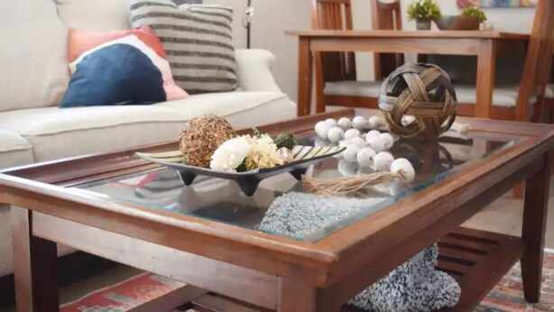 Una sala de estar con una mesa de centro de vidrio, un sofá y una mesa de comedor con sillas.