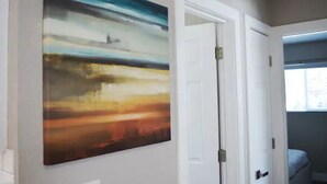 Un pasillo con un cuadro abstracto grande en la pared, una puerta blanca y una ventana que da a vistas del exterior.