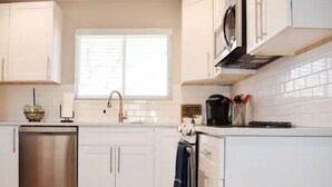 Una cocina moderna con armarios blancos, lavavajillas de acero inoxidable, microondas y cafetera.