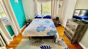 Une chambre à coucher avec un lit, une télévision, une commode, une fenêtre et un ventilateur.
