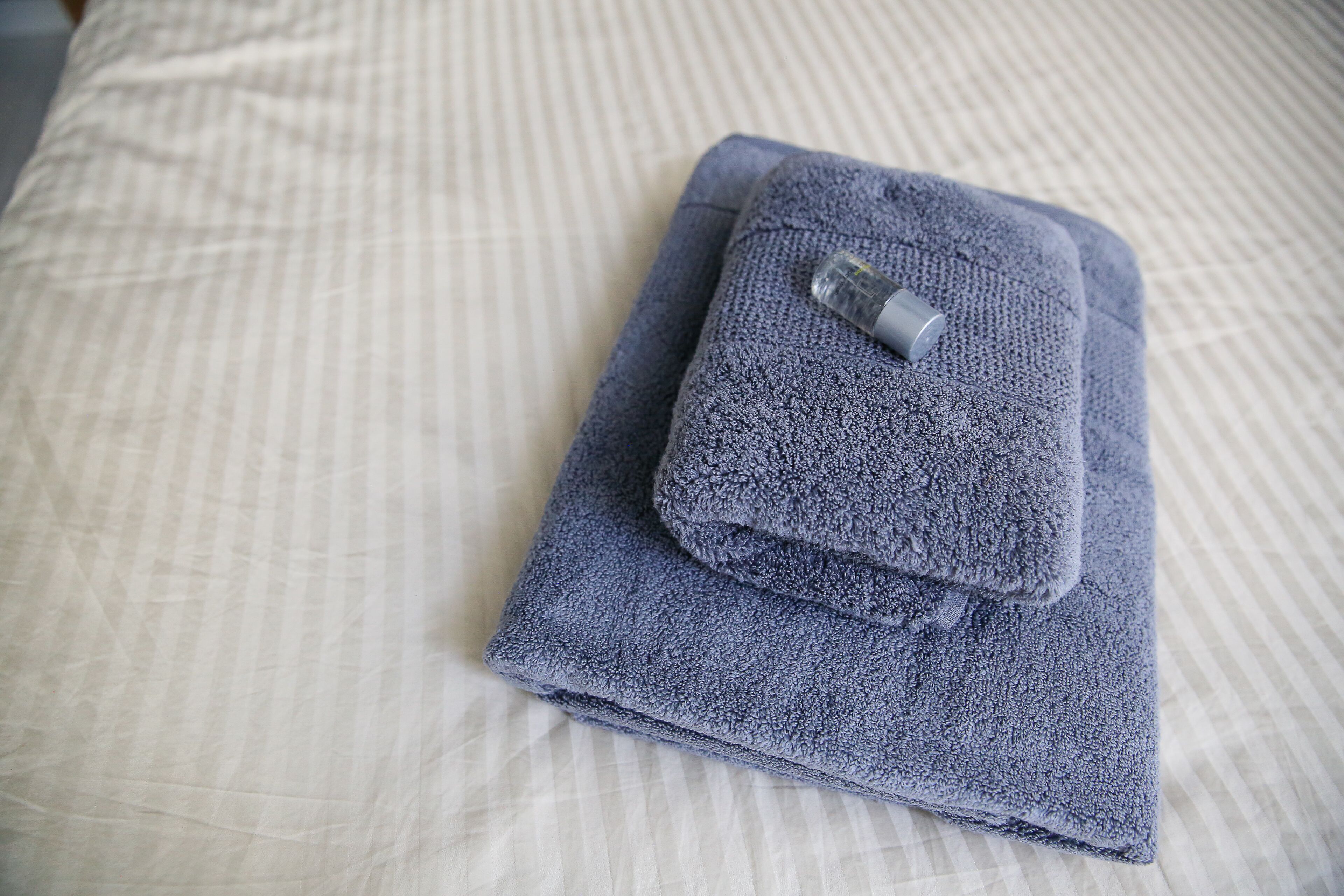 Una toalla azul doblada con orden sobre una cama con estampado a rayas.