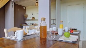 Una mesa de desayuno dispuesta con tazas blancas, una botella de vidrio, una botella amarilla, una manzana verde y un croissant.