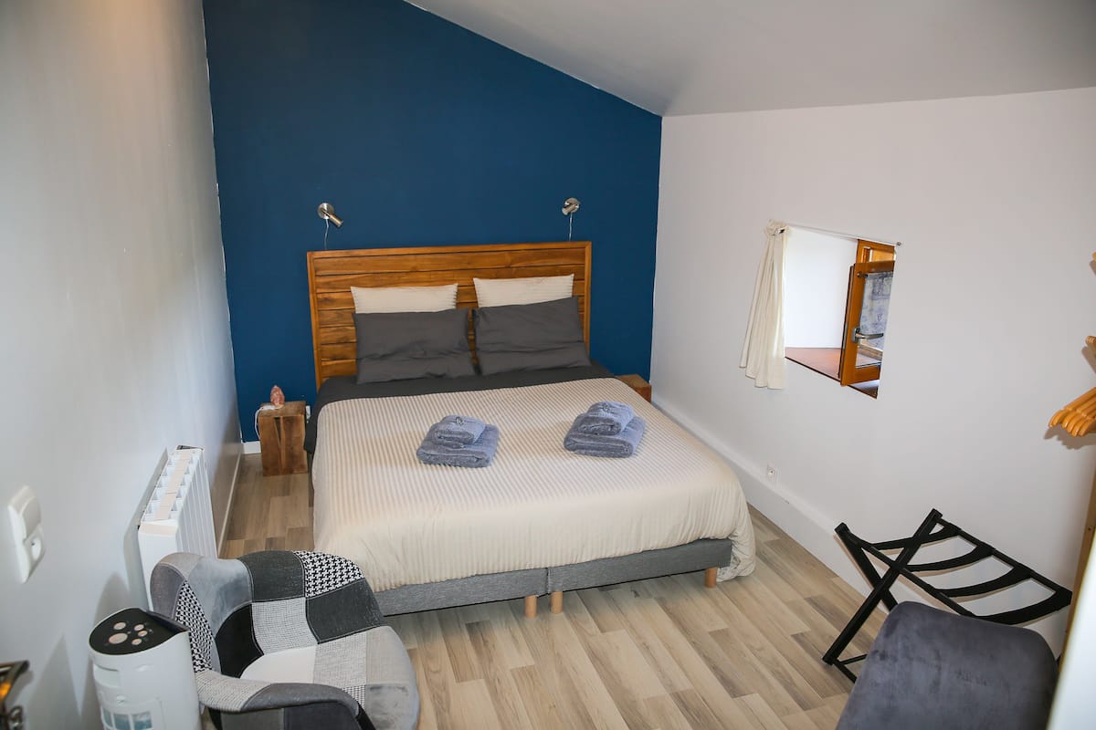 Un dormitorio con cama, una silla, una mesita y un espejo en la pared.