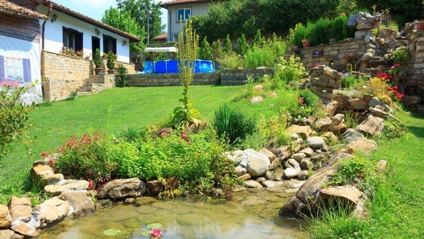 A garden with a pond, stone walls, and a variety of plants and flowers.