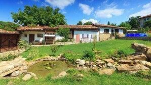 A rustic house with a tiled roof, a small pond, and a well-maintained garden.