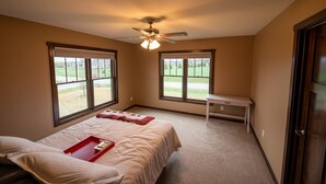 Une chambre à coucher avec un lit, un ventilateur de plafond et deux fenêtres donnant sur un paysage verdoyant.