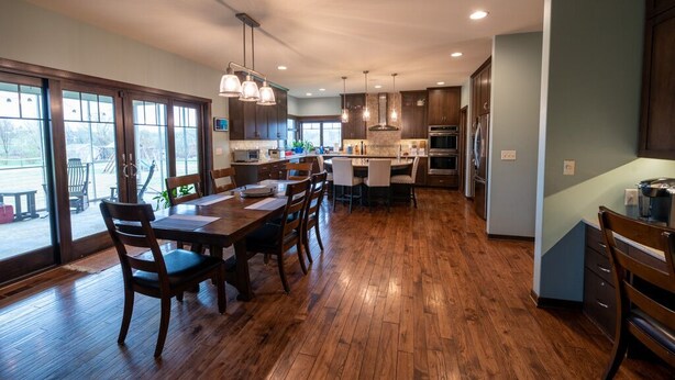 Une cuisine spacieuse avec un plancher en bois, un coin repas avec une table et des chaises, et une vue dégagée grâce à de grandes fenêtres.