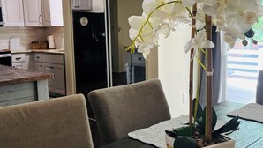 A dining table with a potted orchid centerpiece, a dark wooden table, and a white placemat. - Maplewood Haven (Daphne)