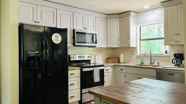 A kitchen with white cabinets, a black refrigerator, a microwave, a stove, and a wooden countertop. - Maplewood Haven (Daphne)