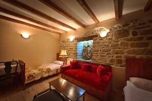 Una habitación acogedora con pared de piedra, un sofá rojo, un banco de madera y una cama.