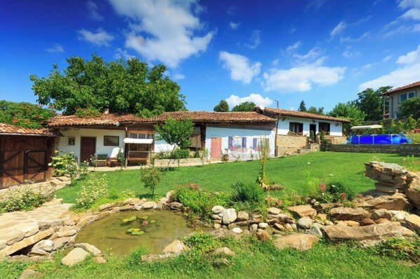 A rustic house with a tiled roof, a small pond, and a well-maintained garden.