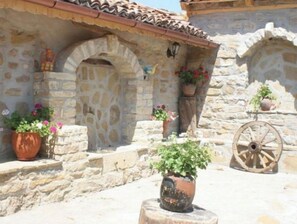 A stone building with arched doorways, potted plants, and a wooden wheel.