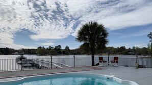 Una piscina amb vora corba, una palmera i vista a un llac amb un pont i cases al fons.