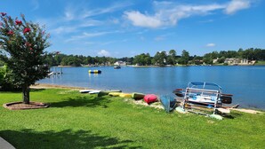 Vista sobre un llac amb una zona enjardinada, un moll amb barques i un arbre amb flors roses.