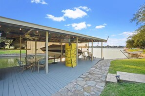 A covered outdoor seating area with a table and chairs, a yellow pillar, and a view of a body of water. - Shorhaus, Gorgeous Main Body Lake Retreat (Granbury)