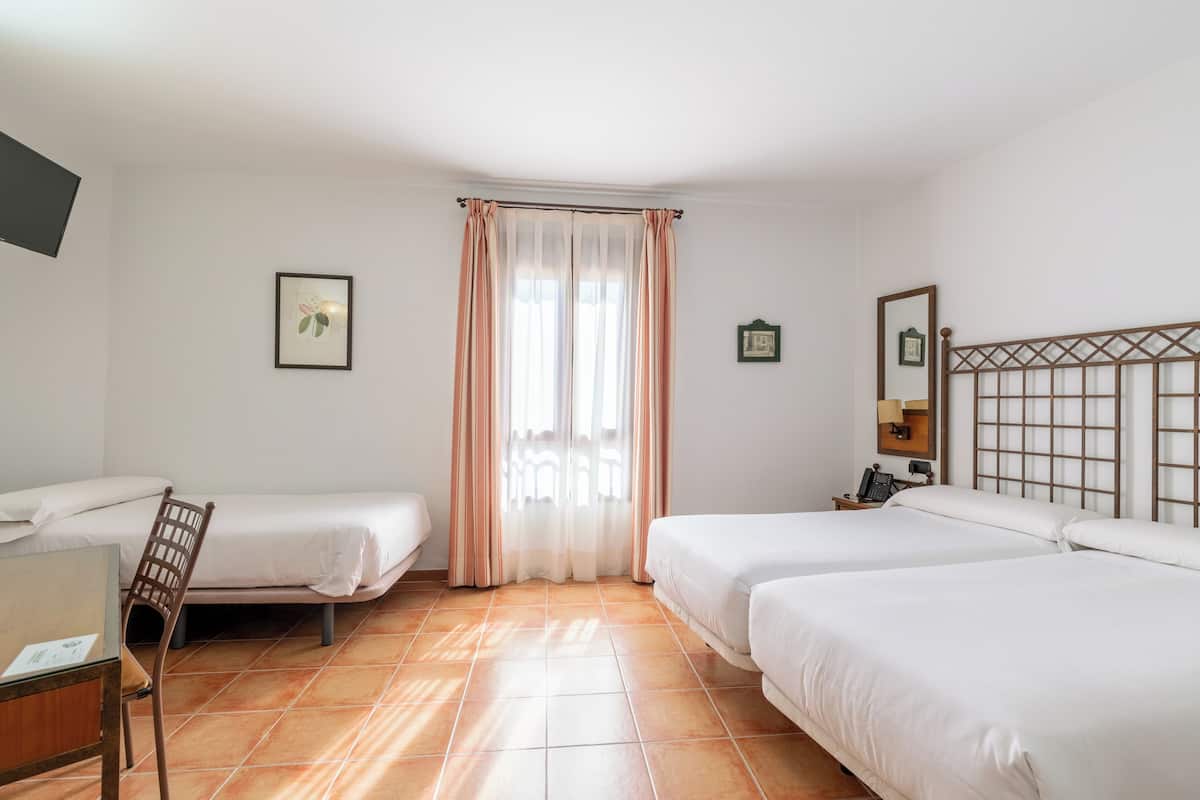 A hotel room with two single beds, a desk with a chair, a small table, a mirror, and a window with curtains.