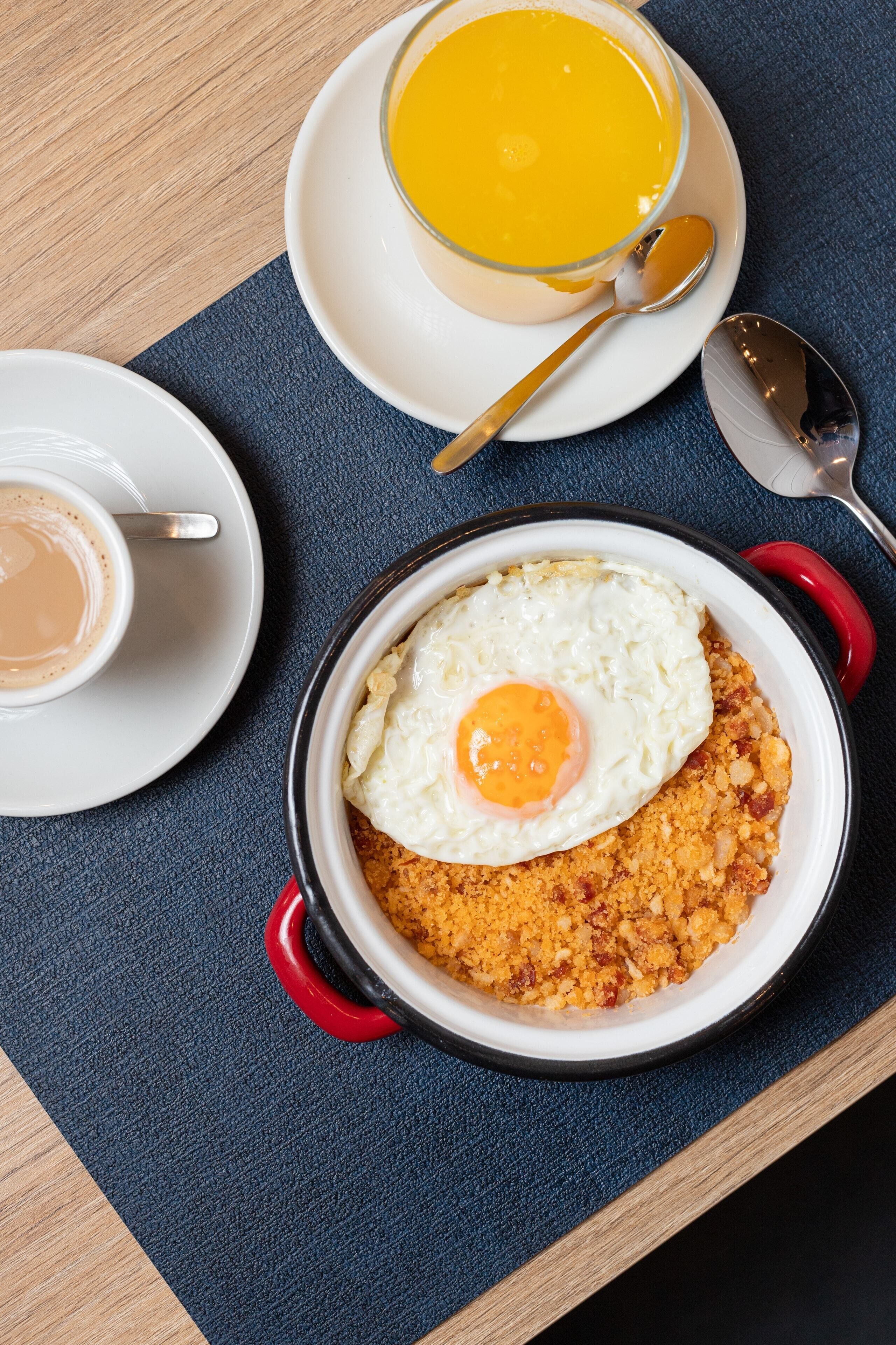 Ein Frühstückstisch mit einer Suppenschüssel, einer Kaffeetasse und einem Teller mit Spiegelei auf zerbröselter Nahrung.