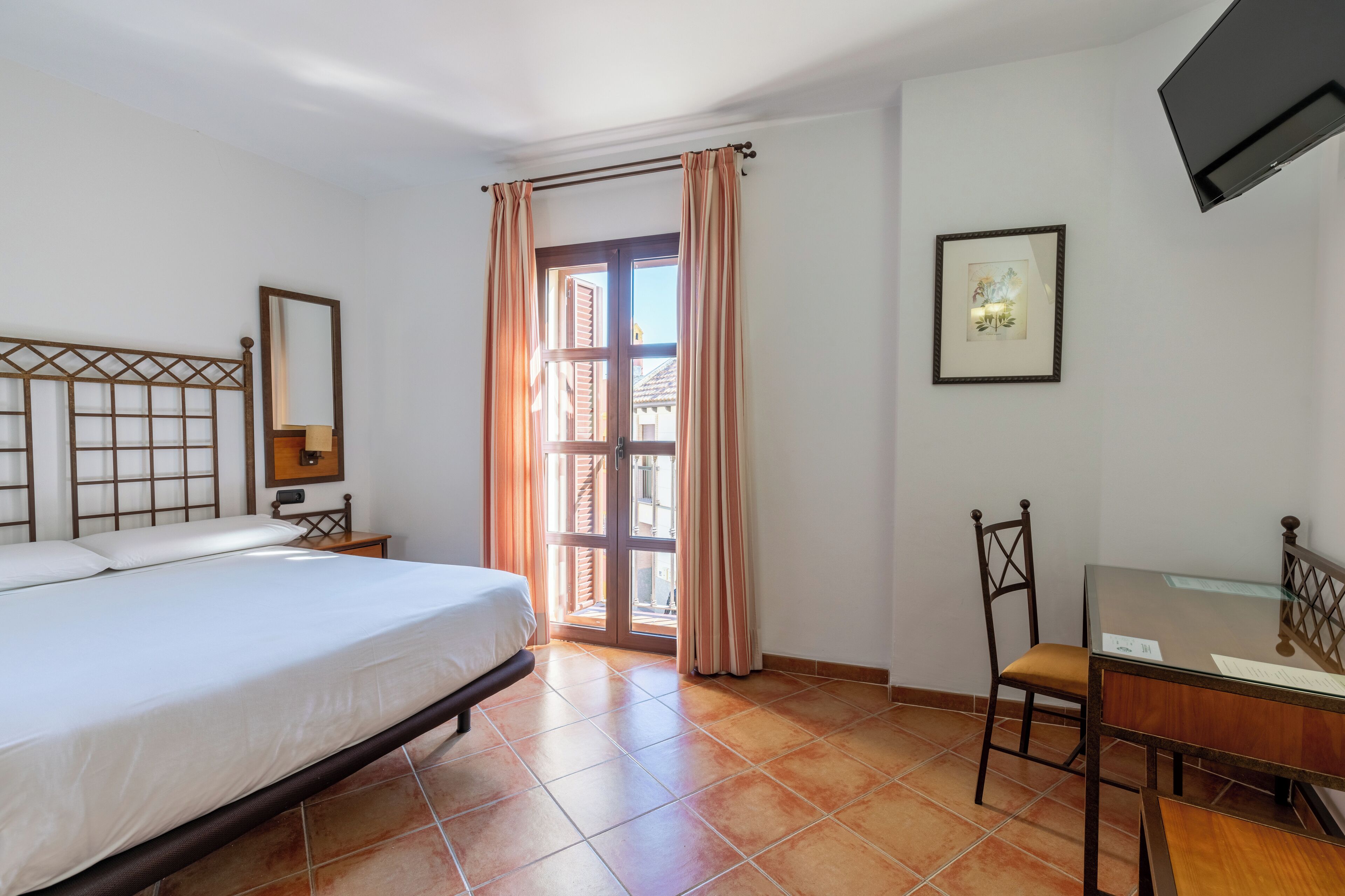 Une chambre d’hôtel avec un lit, un bureau, une chaise, une télévision et une fenêtre avec des rideaux.