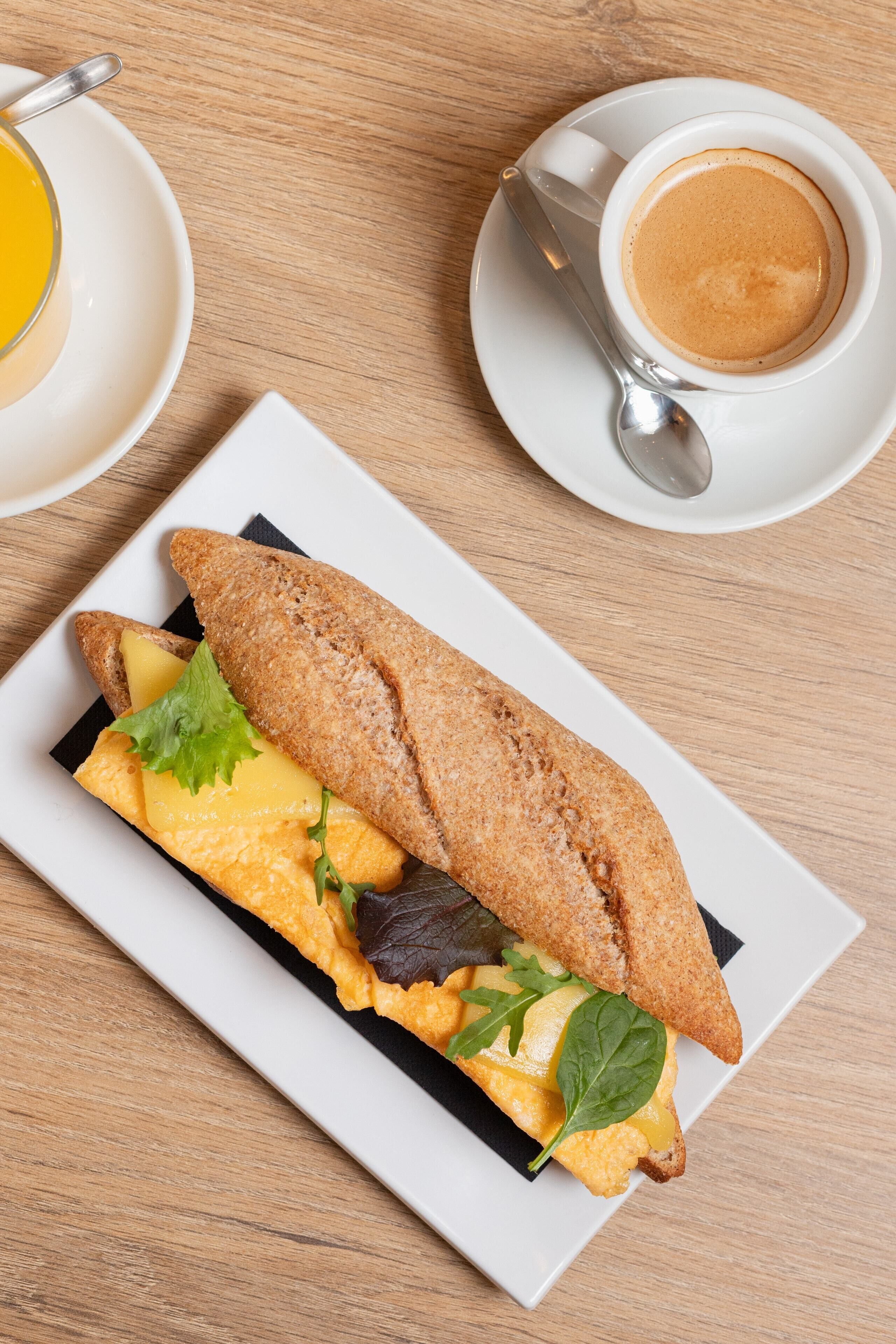 Un sandwich sur une assiette blanche, avec une tasse de café posée sur une soucoupe à côté.