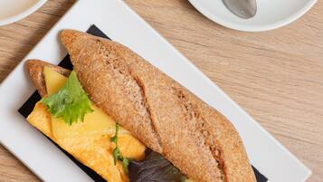 Un sandwich sur une assiette blanche, avec une tasse de café posée sur une soucoupe à côté.
