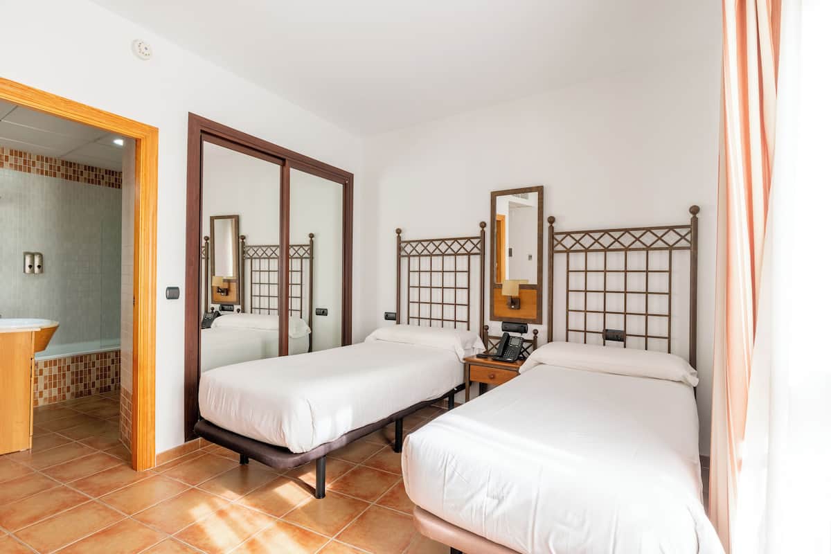 A hotel room with two beds, a bathroom, and a shower area.