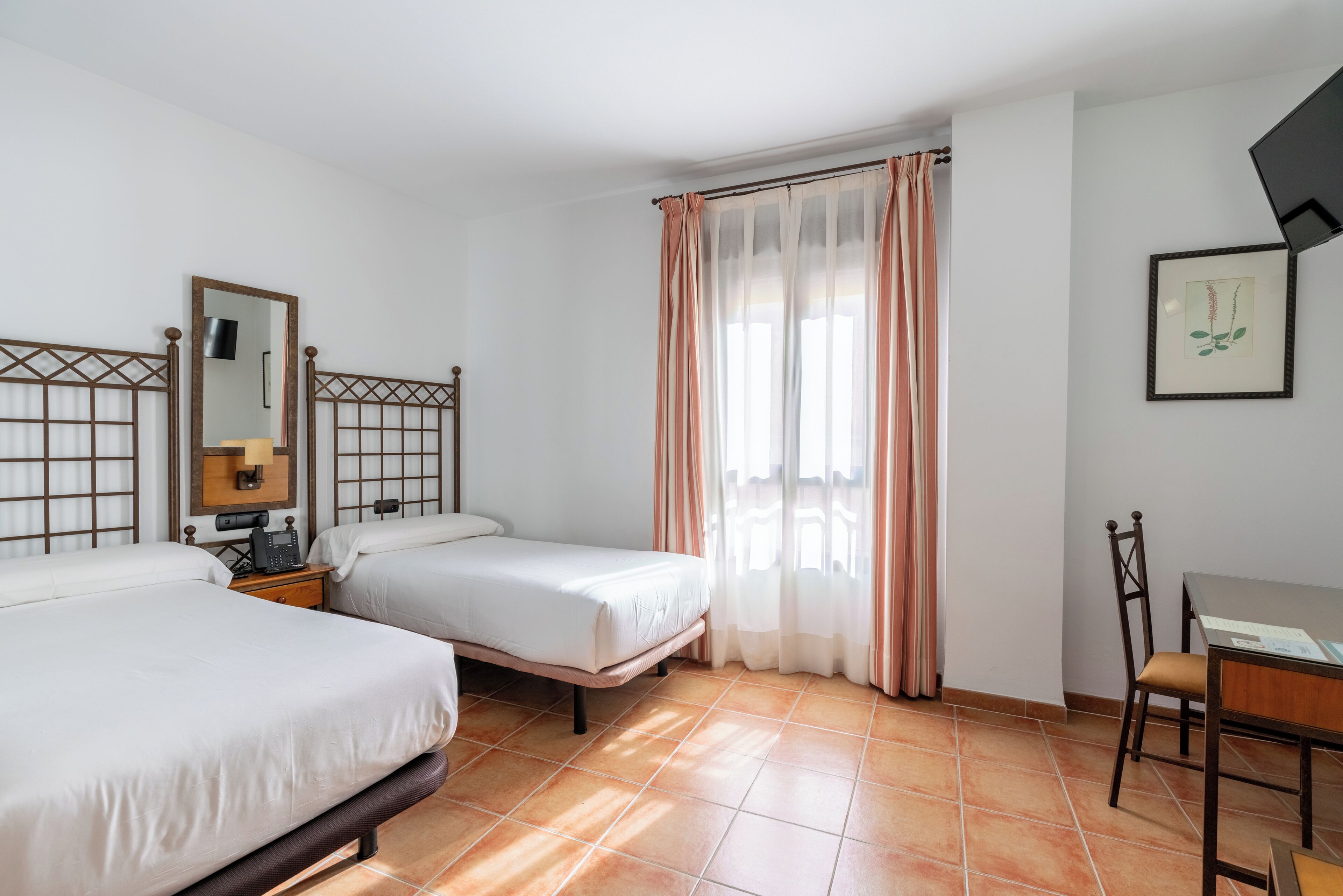 A hotel room with two beds, a desk, a chair, a mirror, and a window with curtains.