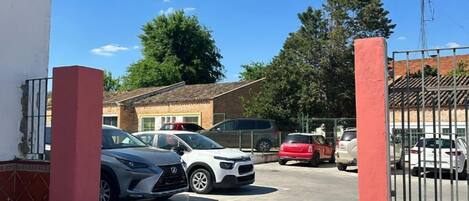 Un estacionamiento con varios autos, un edificio con una columna roja y un cielo azul despejado.