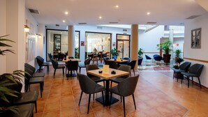 A spacious lobby with multiple seating areas, including tables and chairs, and a visible restaurant in the background.