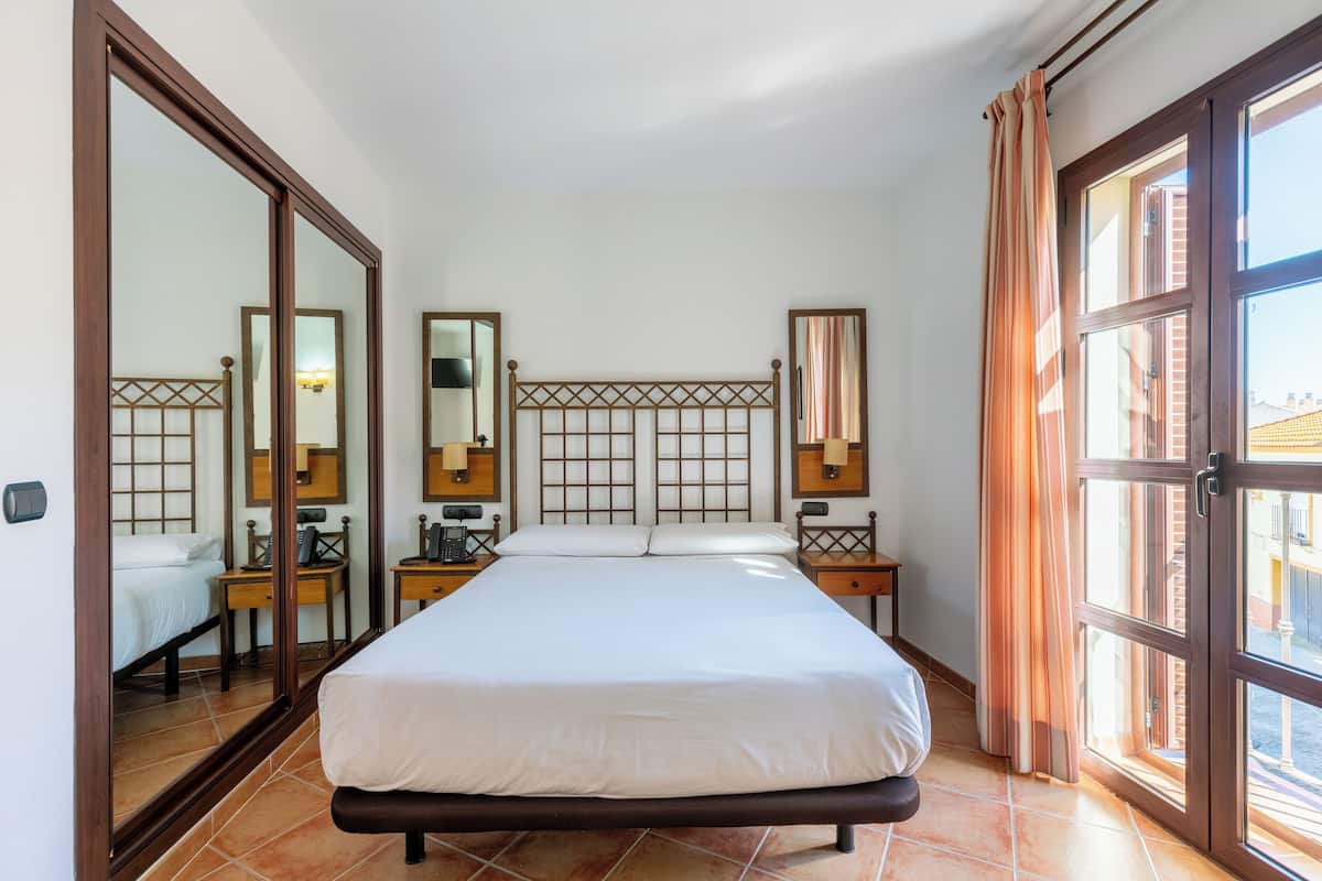 A hotel room with a large bed, a wardrobe, a desk, and a window with curtains.