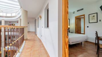 Un pasillo de hotel con techo alto, barandal de madera, una cama y una puerta de madera.
