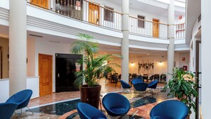 A spacious lobby with a high ceiling, marble flooring, and blue chairs arranged around a central table.