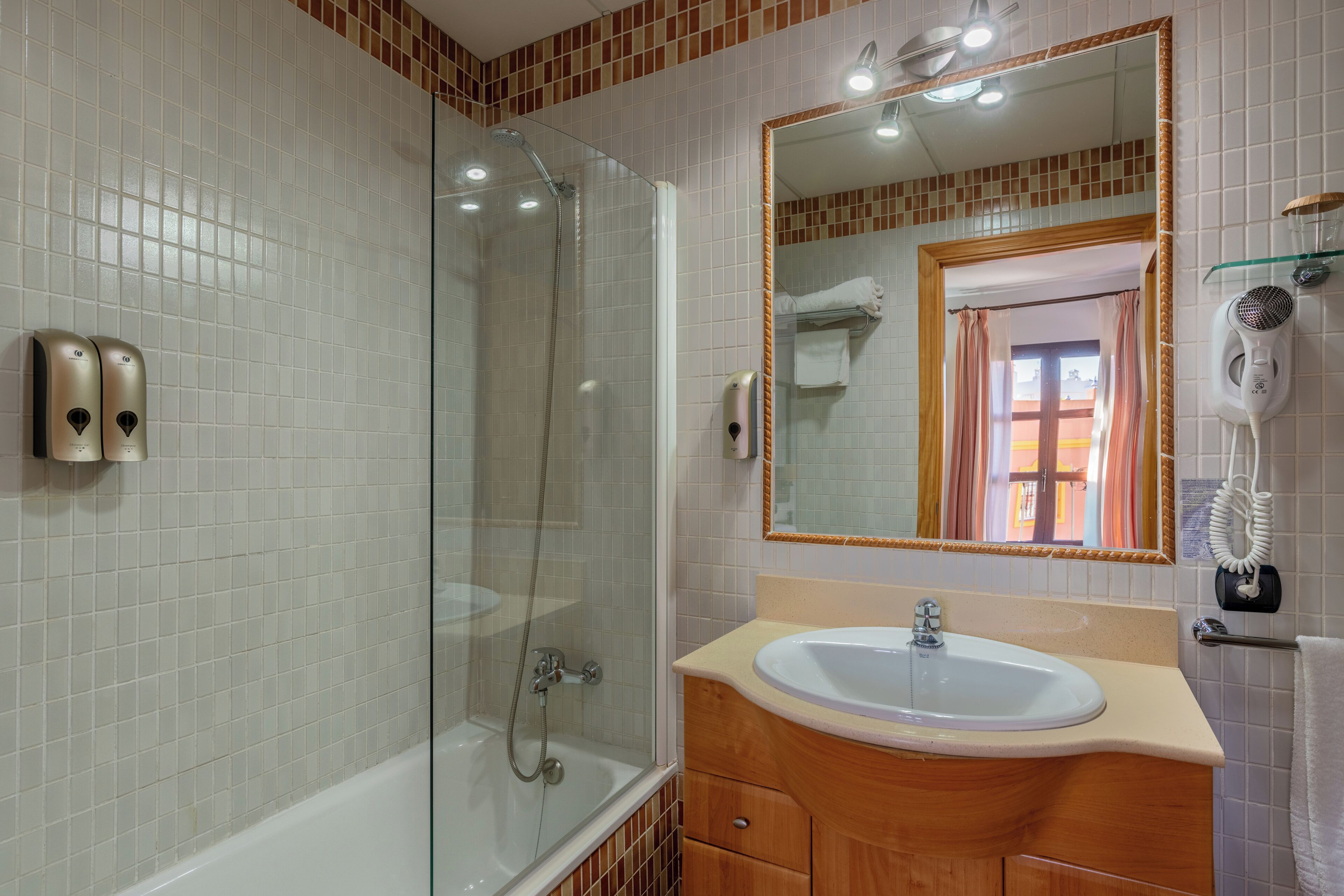 Un baño moderno con ducha envuelta en vidrio, lavabo con tocador de madera y un espejo grande.