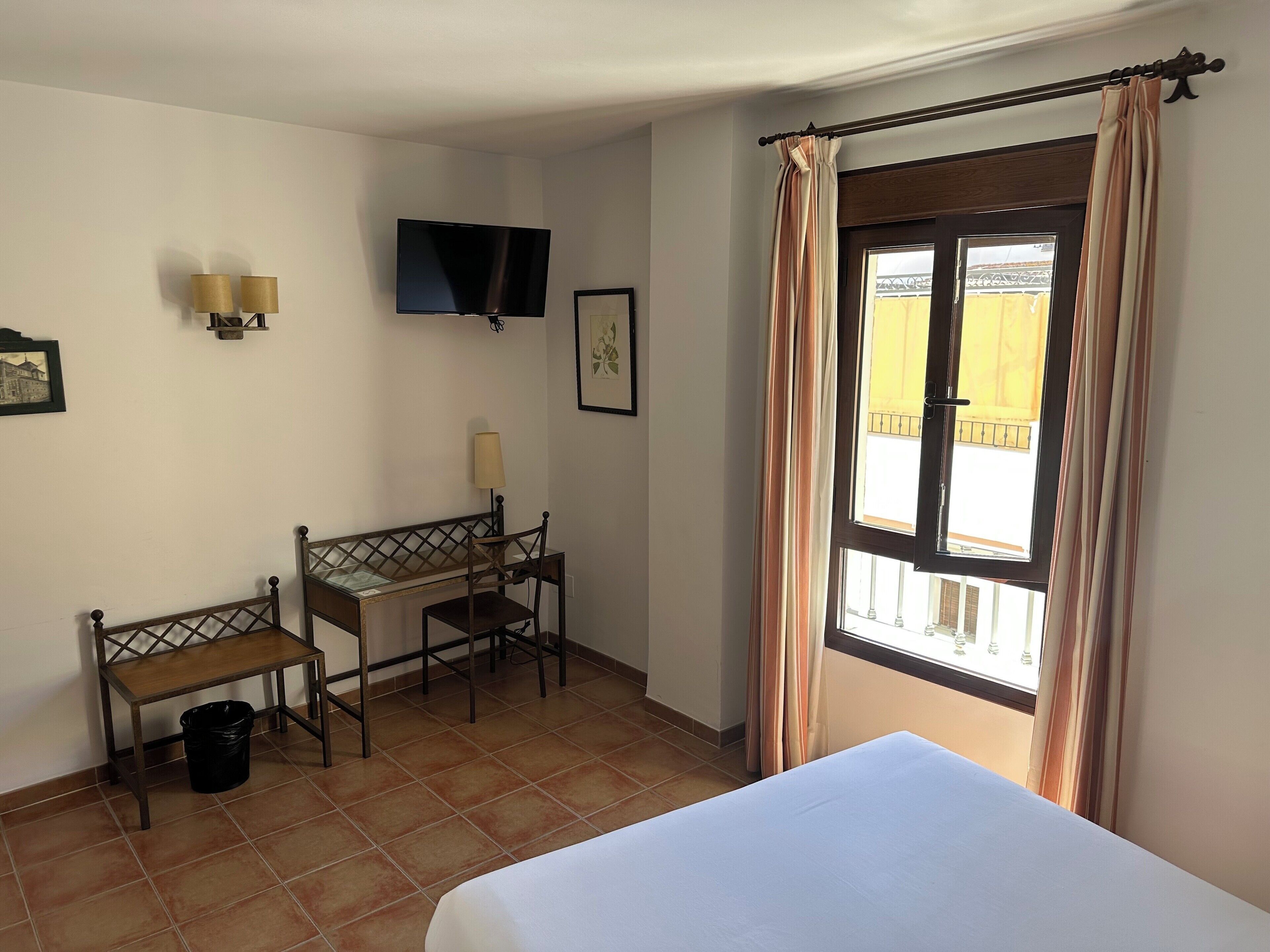 Une chambre comprenant un lit, un bureau avec une chaise, un téléviseur fixé au mur et une fenêtre avec des rideaux.