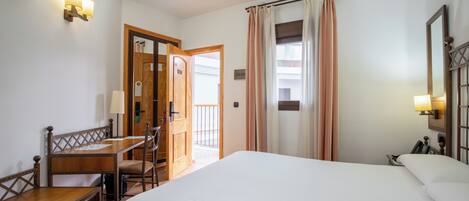 A hotel room with a bed, a desk, a chair, a small table, and a bathroom door.