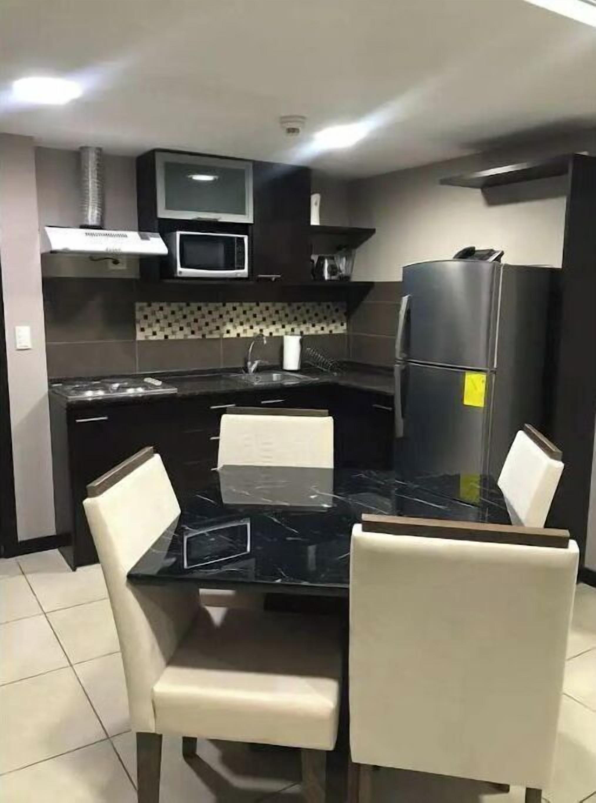 A modern kitchen with a black countertop, white chairs, a microwave, and a refrigerator.
