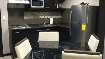 A modern kitchen with a black countertop, white chairs, a microwave, and a refrigerator.