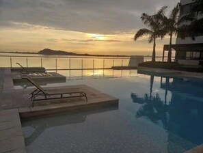 Un espace piscine avec des chaises longues et une vue sur le coucher de soleil au-dessus de l’eau.