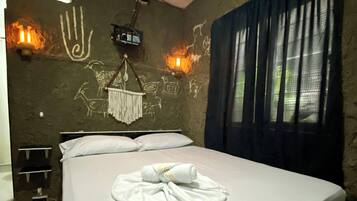 Una cama individual con una toalla doblada con cuidado, una lámpara de pared y una obra de arte hecha a mano en la pared.